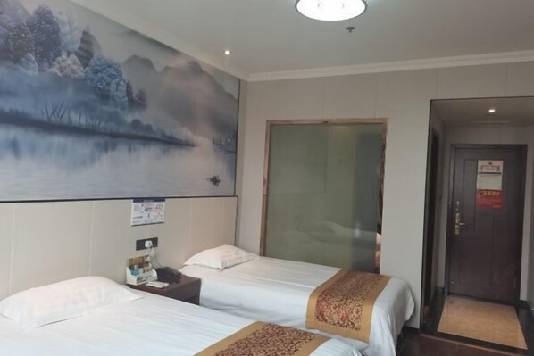 Habitación de hotel con dos camas, un cuadro grande en la pared, una puerta con panel de vidrio y una señal visible en la pared.