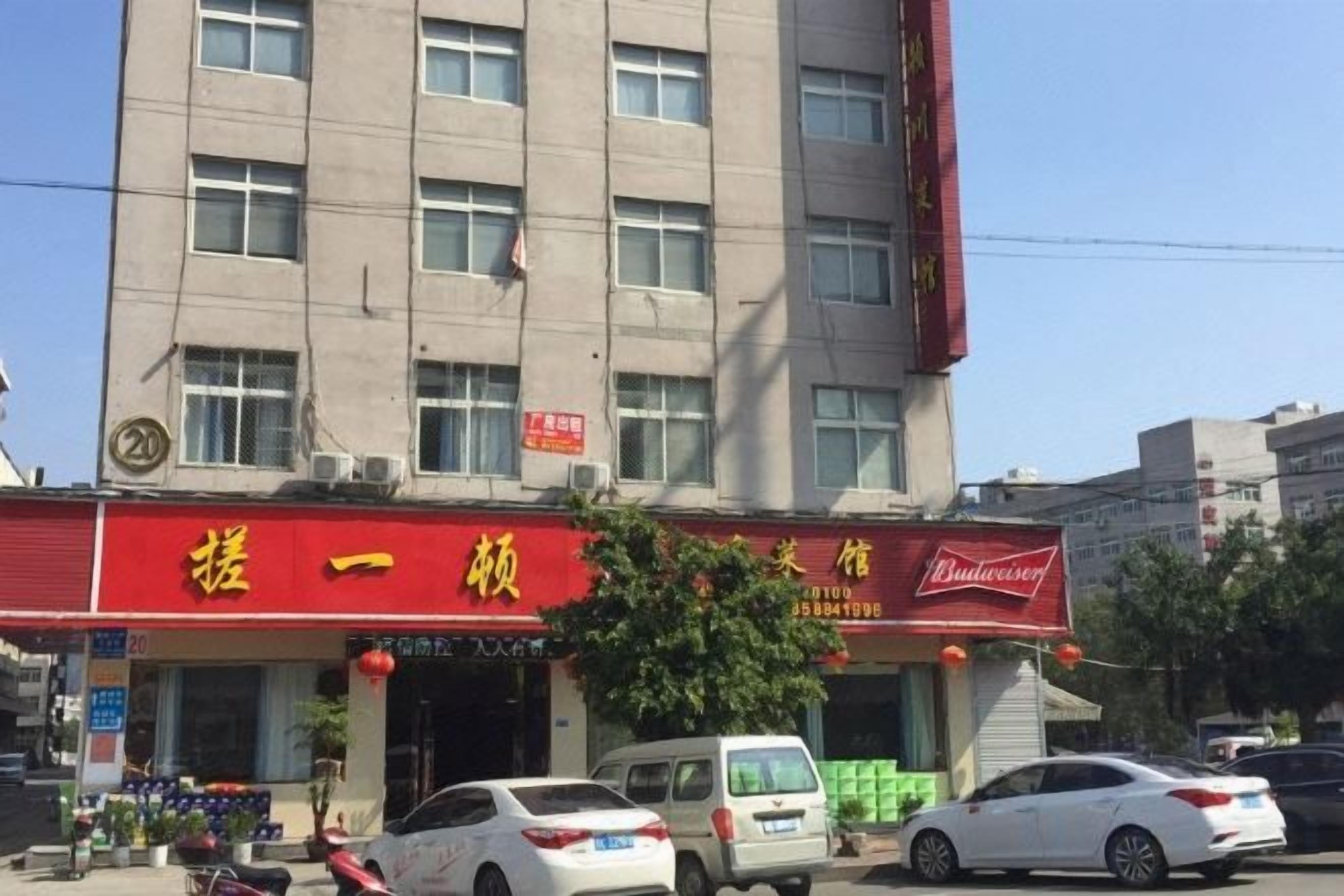 Un edificio con un tendone rosso e un'insegna per un hotel. Diverse auto sono parcheggiate davanti.