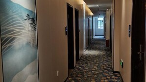 Ein Hotelgang mit Teppichmuster, Türen und einer Wand mit einem Wandgemälde zum Thema Natur.