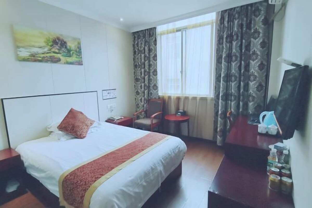 Habitación de hotel con cama, una silla, una mesita, televisor y ventana con cortinas.