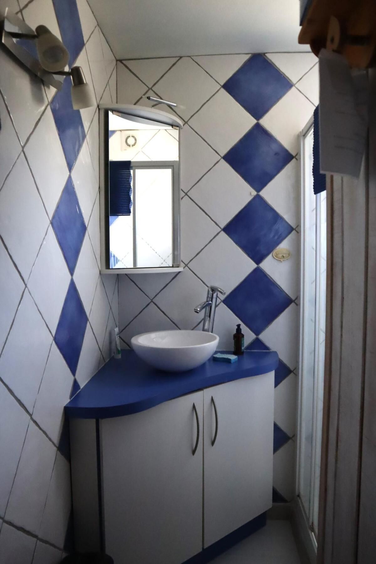Une salle de bain avec un lavabo blanc, un miroir et un mur recouvert de carreaux bleus et blancs.