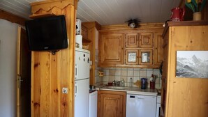 A compact kitchen with wooden cabinets, a white refrigerator, a dishwasher, and a mounted television. - 2nd floor, balcony, parking, tv, ski locker, 40m², Valloire (Valloire)