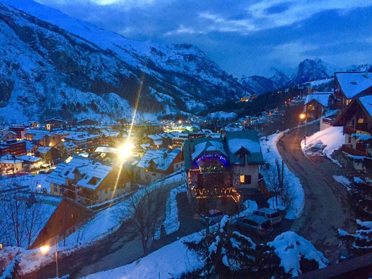 A snow-covered village at dusk with illuminated buildings and a winding road.