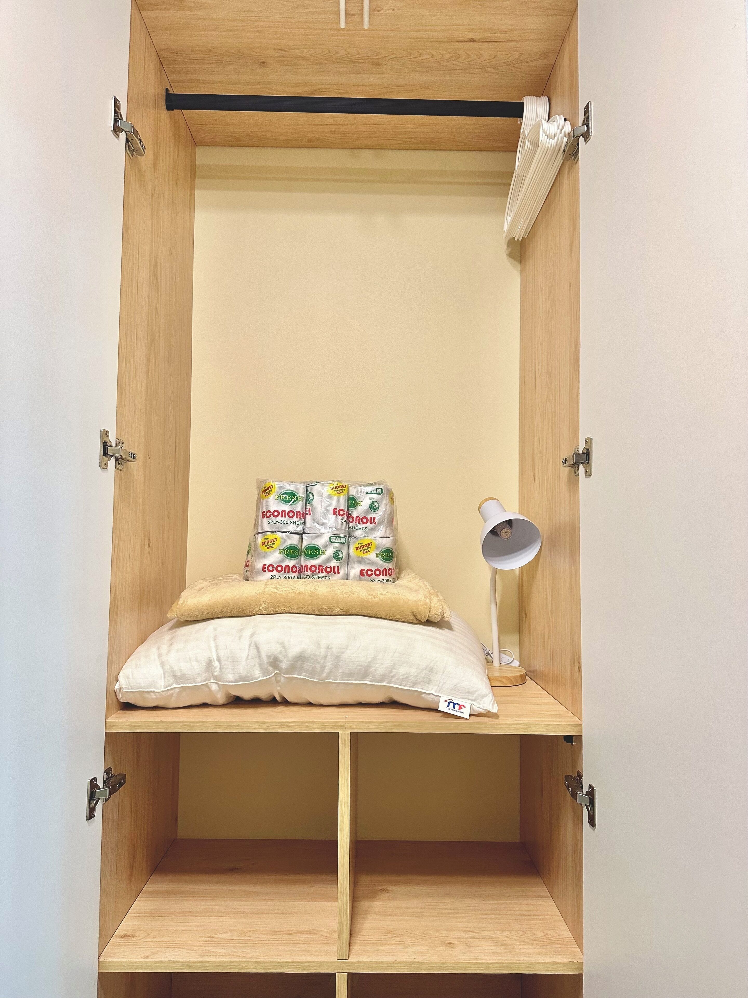 Un armario de madera con un estante en la parte inferior, una lámpara colgante y dos almohadas.