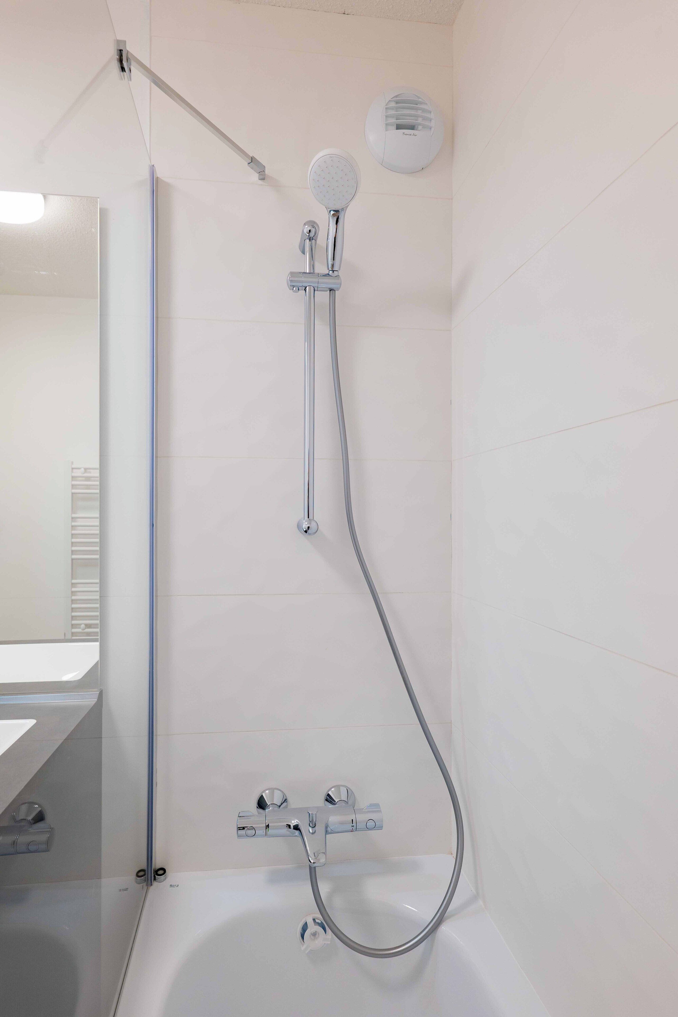 A modern bathroom with a bathtub, a shower with a handheld showerhead, and a wall-mounted toilet.