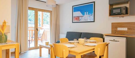 A modern kitchen with a microwave, a sink, and a dishwasher. There is a dining area with a table set for two, and a sofa in the background.