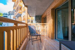 Un balcon en bois avec une chaise, un mur en pierre et une vue sur d’autres bâtiments.