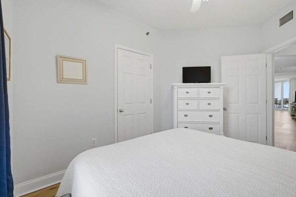 A bedroom with a large bed, a dresser, a television on top, and two white doors. - Palacio 405 (Pensacola)