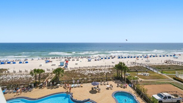 A beach view from a hotel balcony with a swimming pool, lounge chairs, and a sandy beach area. - Palacio 405 (Pensacola)
