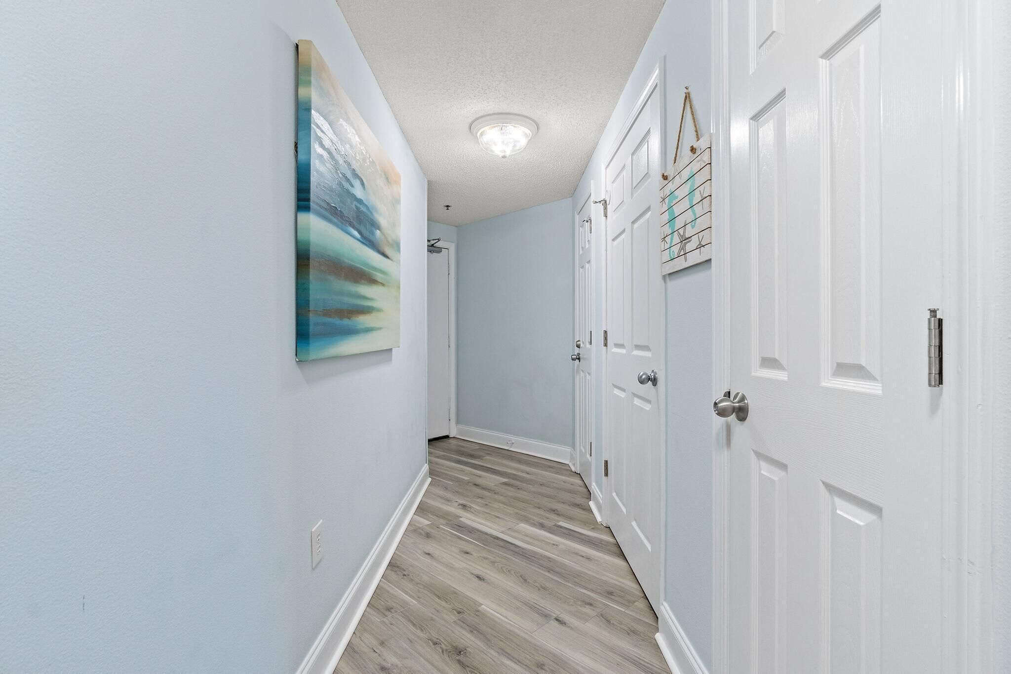 A hallway with light blue walls, a wooden floor, and white doors.