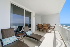 A balcony with a table and chairs, a lounge chair with a cushion, and a view of the ocean. - Palacio 405 (Pensacola)