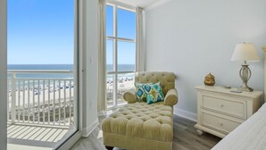 A bedroom with a view of the beach, a tufted armchair, a bedside table with a lamp, and a window with curtains. - Palacio 405 (Pensacola)