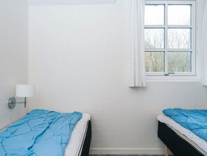 A room with two beds, a window with curtains, and a wall-mounted lamp.