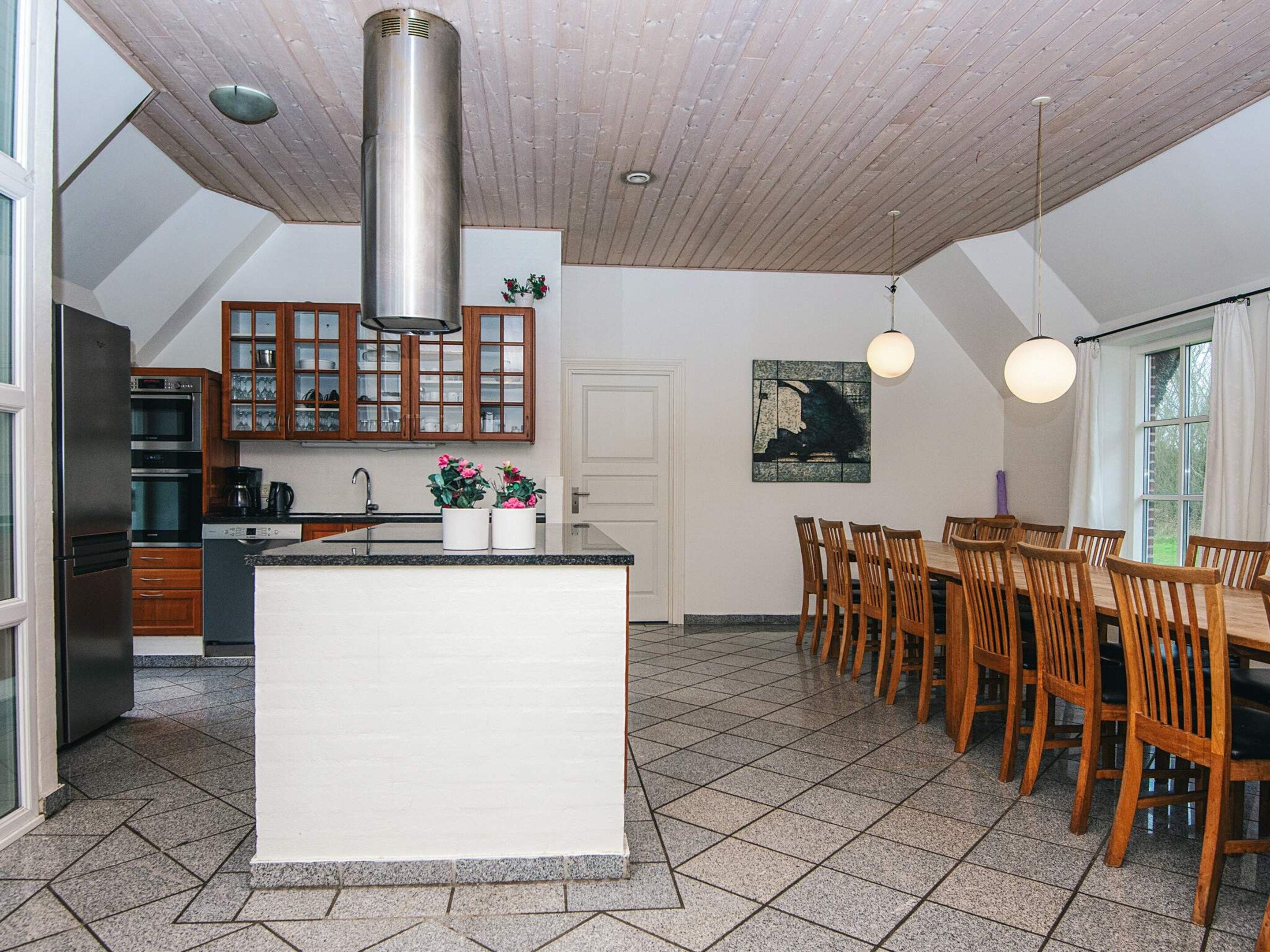 A modern kitchen with a central island, wooden cabinets, and a dining area with a large table and chairs.