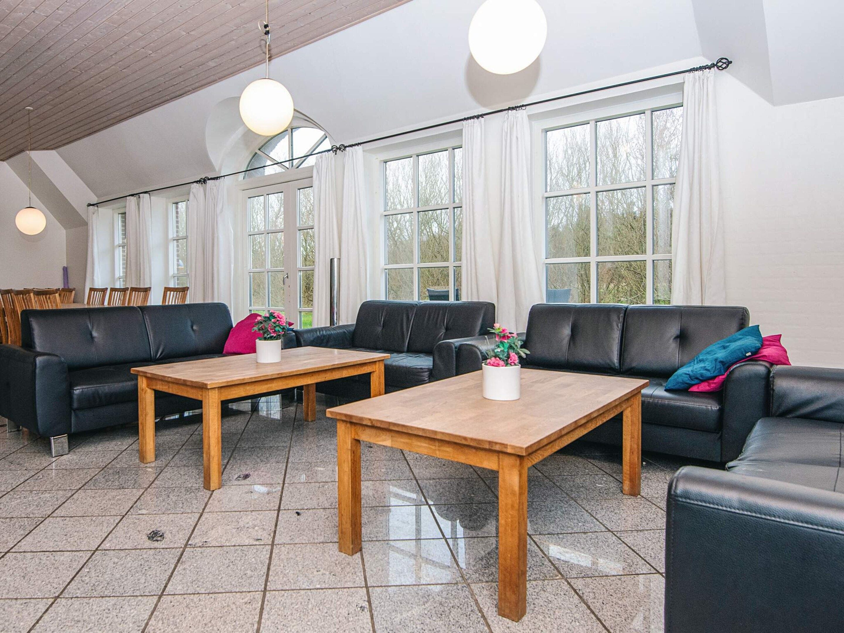 A spacious room with a high ceiling, large windows, and a black leather sofa set.