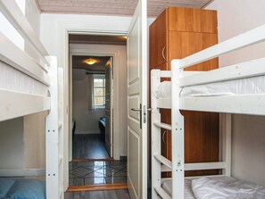 Une chambre avec des lits superposés, une armoire en bois et une porte donnant sur un couloir.