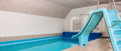 An indoor swimming pool with a blue slide, tiled walls, and a window.