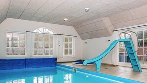 Une piscine intérieure avec un toboggan bleu, de grandes fenêtres et un plafond carrelé.