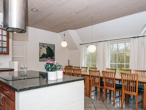 A kitchen with a granite countertop, wooden cabinets, and a dining area with wooden chairs and a table. - 4 Star Holiday Home in Ulfborg (Ulfborg)