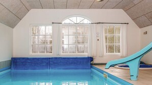 Une piscine intérieure avec un toboggan bleu, de grandes fenêtres et un banc le long du mur.