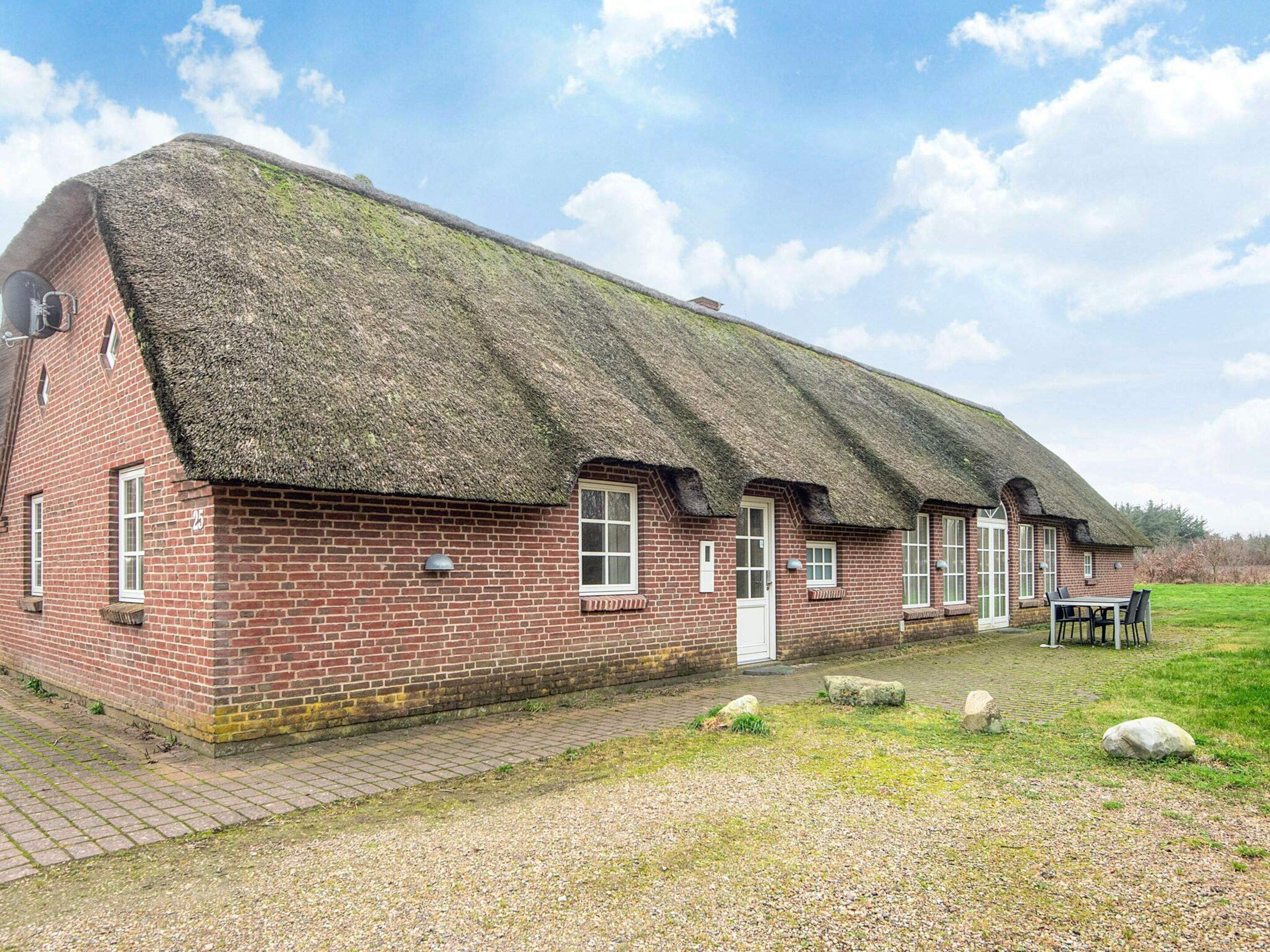 A traditional brick building with a thatched roof, a paved driveway, and a grassy area with a table and chairs.