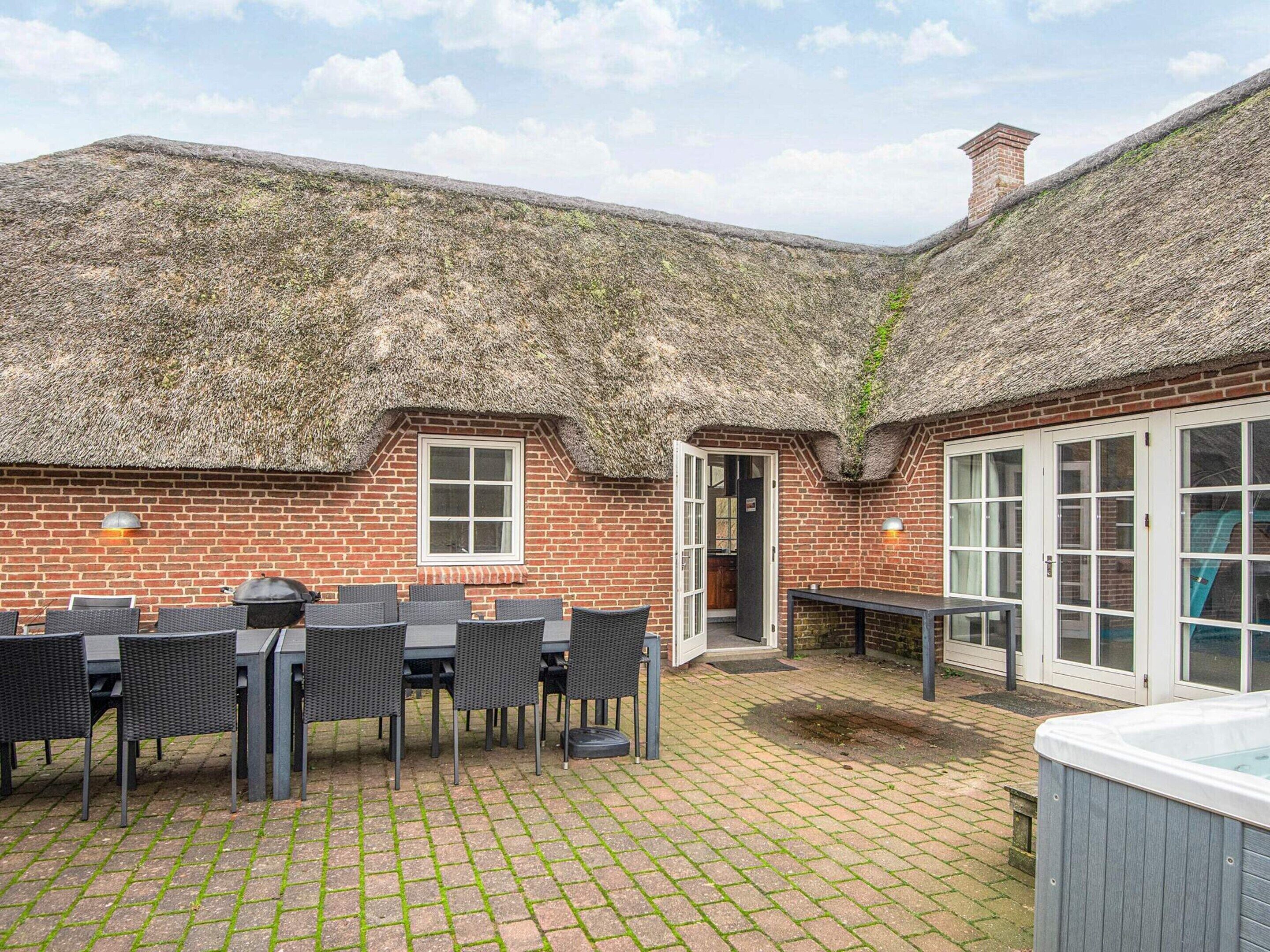 A patio area with a brick wall, a thatched roof, and a hot tub.