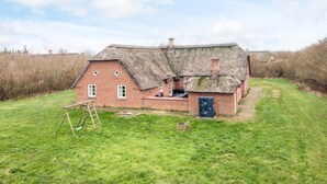 Une maison en briques avec un toit de chaume, une balançoire en bois et un petit jardin.