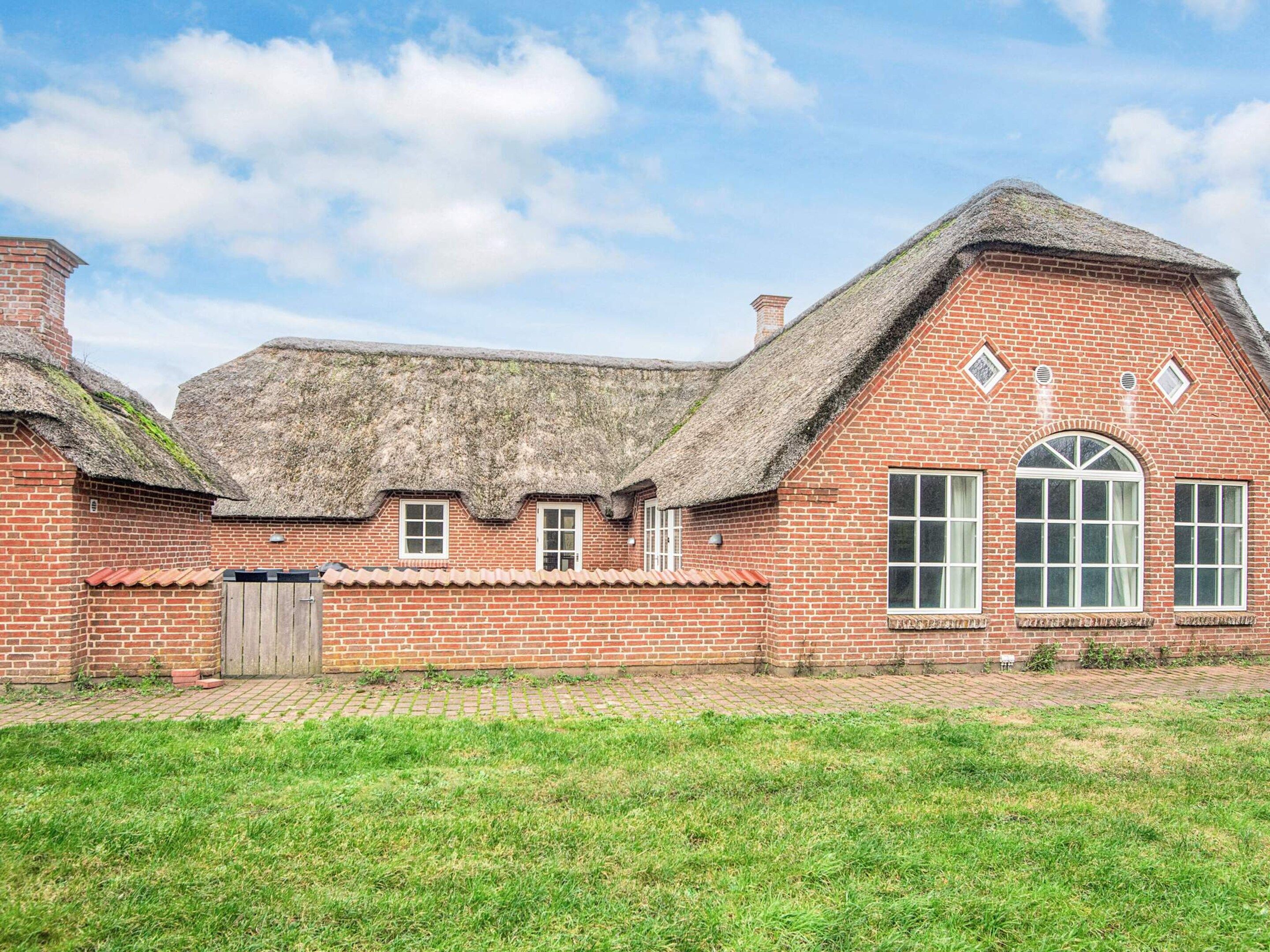 A traditional brick building with a thatched roof, a wooden gate, and a paved pathway leading to the entrance.