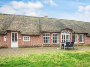 A traditional brick building with a thatched roof, a white door, and a paved courtyard with a table and chairs. - 4 Star Holiday Home in Ulfborg (Ulfborg)