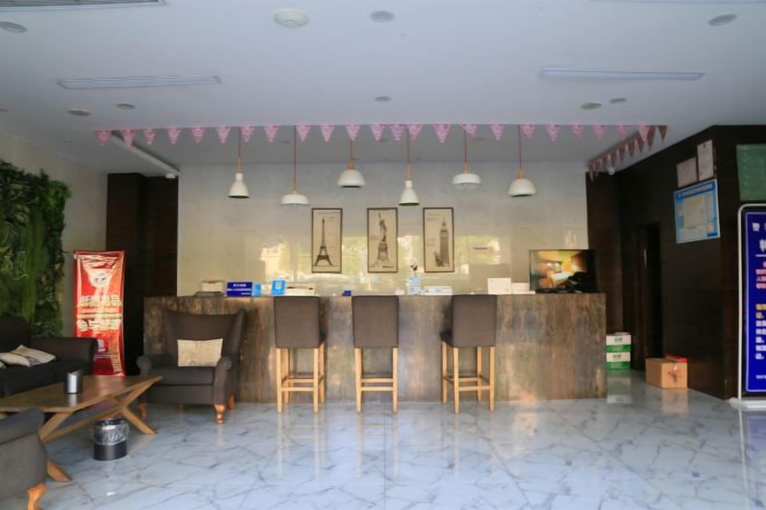 A hotel lobby with a reception desk, bar stools, hanging pendant lights, and a marble floor.
