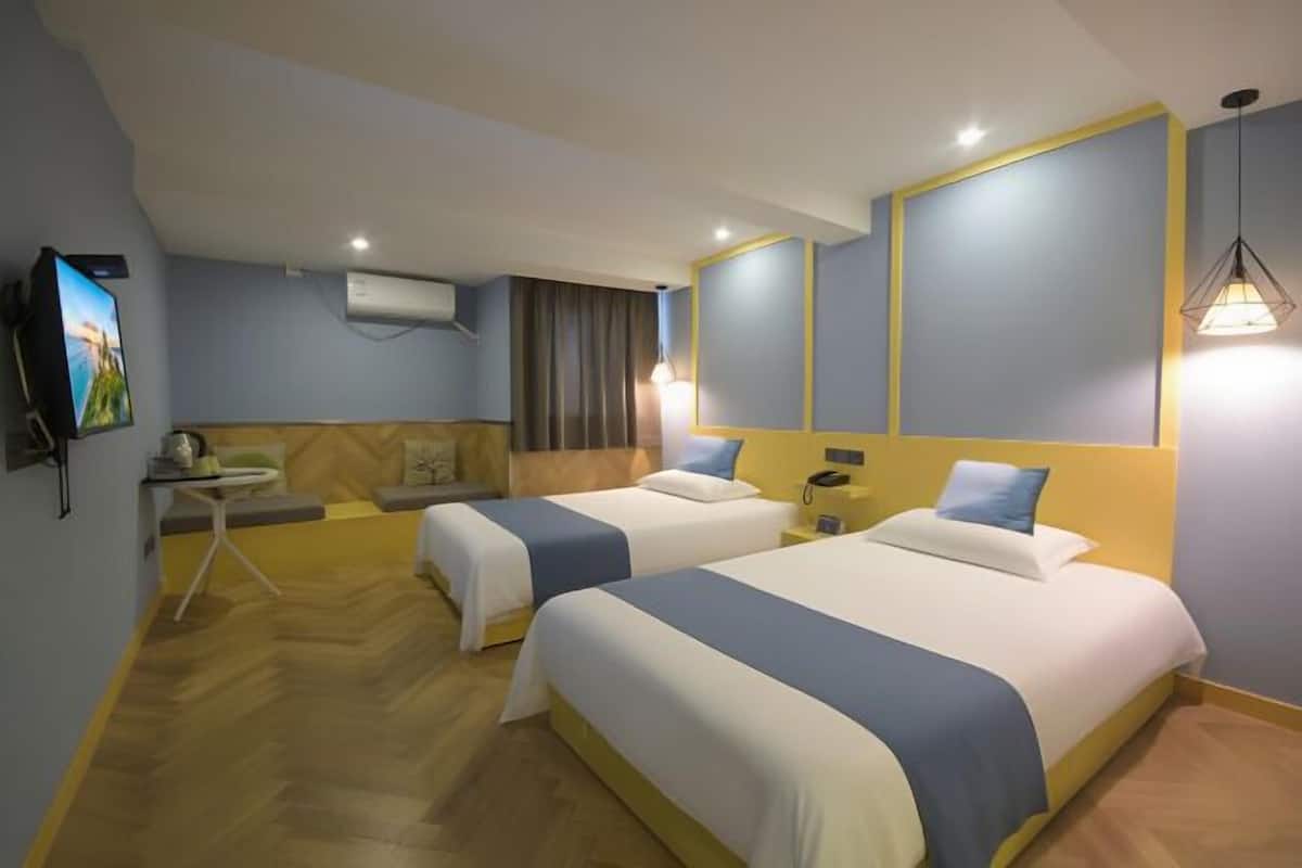 Ein Hotelzimmer mit zwei Betten, einem kleinen Tisch, einem Fernseher und einer Wandklimaanlage.