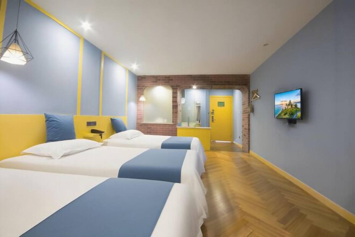 Ein Hotelzimmer mit zwei Betten, einem Fernseher, einem Spiegel und einem durch einen Bogen sichtbaren Badezimmer.