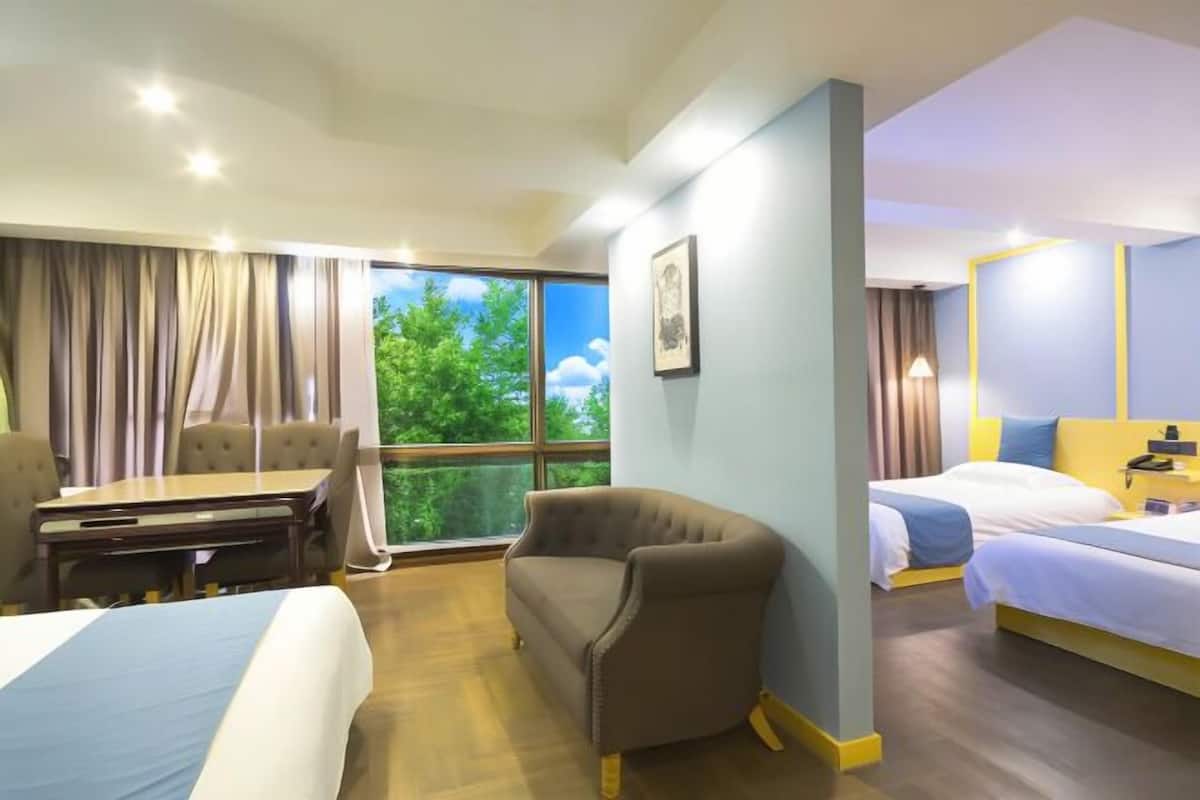 Ein Hotelzimmer mit zwei Betten, einem Sofa, einem Schreibtisch und einem großen Fenster mit Blick auf Bäume.