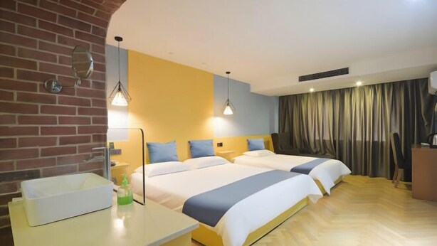Une chambre d’hôtel avec deux lits, une salle de bain avec un lavabo et un mur en briques.