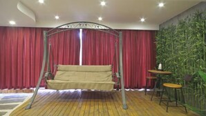 Une pièce avec un lit suspendu, des rideaux rouges, un mur en bambou et une petite table avec des chaises.