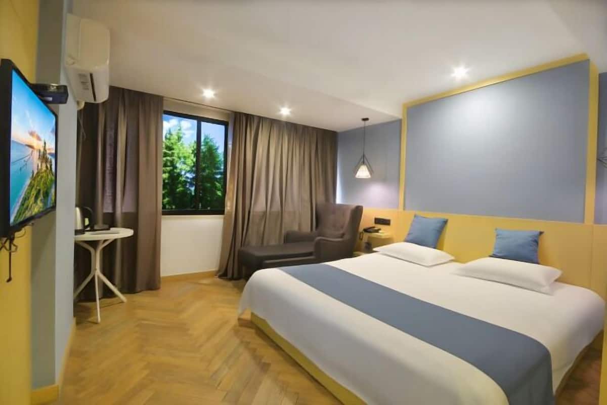 Ein Hotelzimmer mit Bett, Schreibtisch, Stuhl, Fernseher und einem fenster mit Vorhängen.