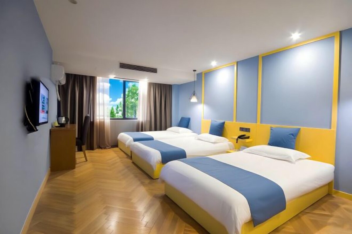 Habitación de hotel con dos camas, televisión, ventana con cortinas y suelo de madera.