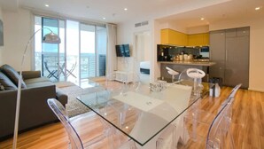 Un appartement moderne doté d’une table à manger en verre, d’un canapé, d’une télévision et d’un balcon offrant une vue agréable.