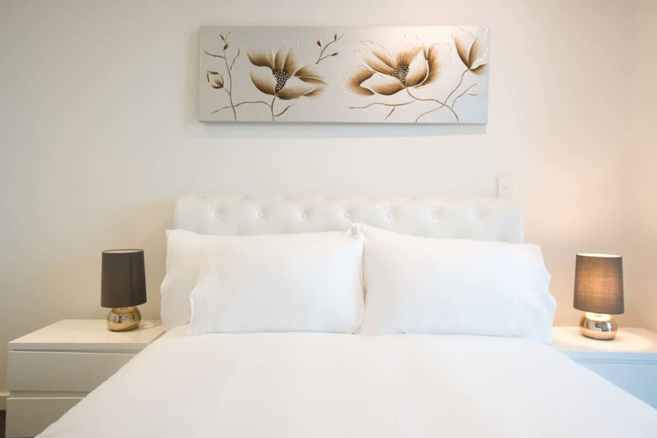 A bedroom with a tufted headboard, white bedding, and two bedside lamps.