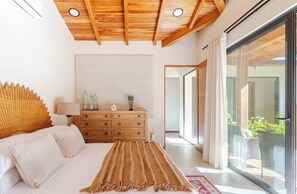 Un dormitorio con cama, cómoda, espejo y puerta corrediza de vidrio a un balcón.