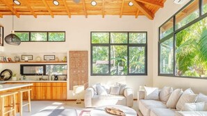 Ein modernes Wohnzimmer mit einem weißen Sofa, einem Couchtisch und einer Küchenzeile mit Holzausbau und einem großen Fenster.