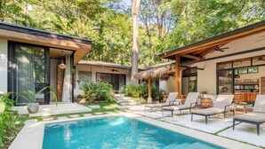 Ein moderner Poolbereich mit klarem Pool, Liegestühlen und einer strohgedeckten Struktur.
