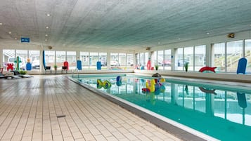 En indendørs swimmingpool med flisegulv, glasvægge og farverigt legetøj.