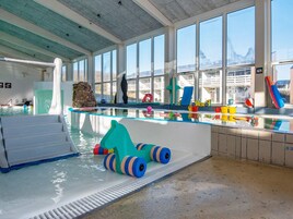 Una piscina interior con barrera de vidrio, pared de piedra y diversos juguetes y equipos de colores.