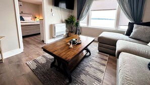 A modern living room with a sofa, a coffee table, a TV mounted on the wall, and a window with curtains.
