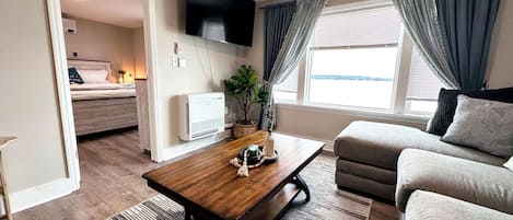 A modern living room with a sofa, a coffee table, a TV mounted on the wall, and a window with curtains.