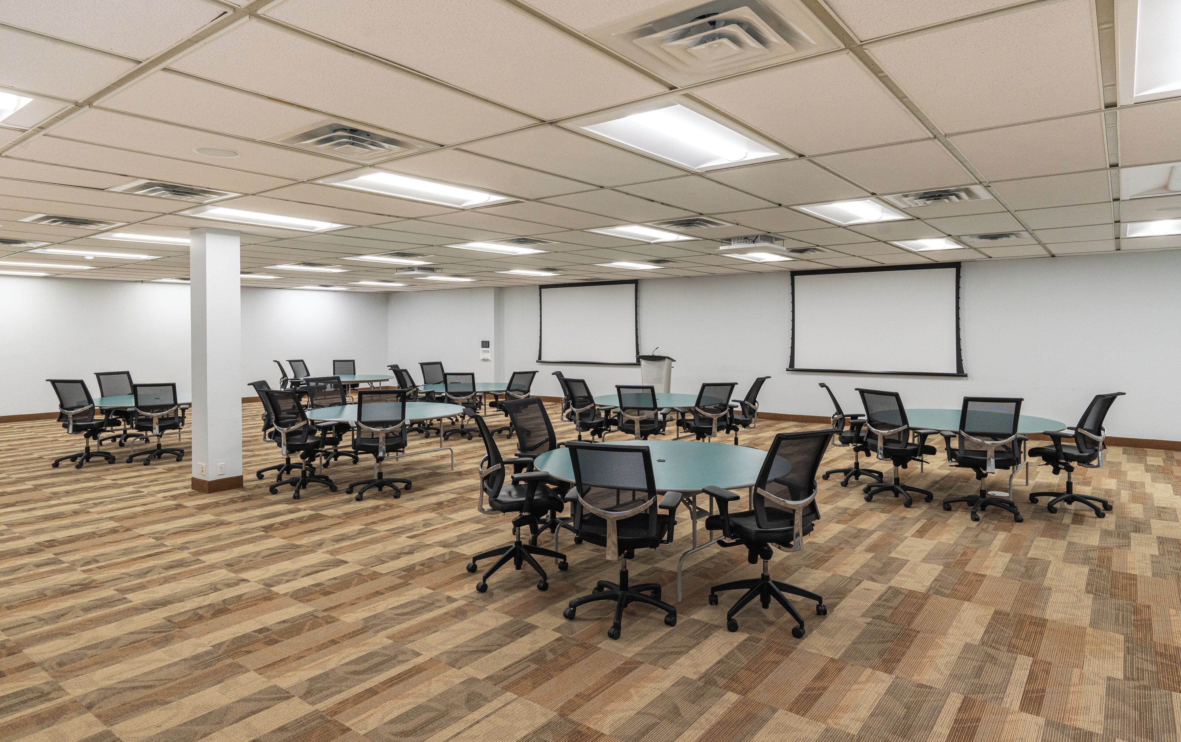 Une salle de conférence dotée de plusieurs tables et chaises, de grandes fenêtres et d’un écran de projection.