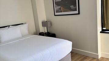A hotel room with a large bed, a bedside table with a lamp, a framed picture on the wall, and a window with curtains.