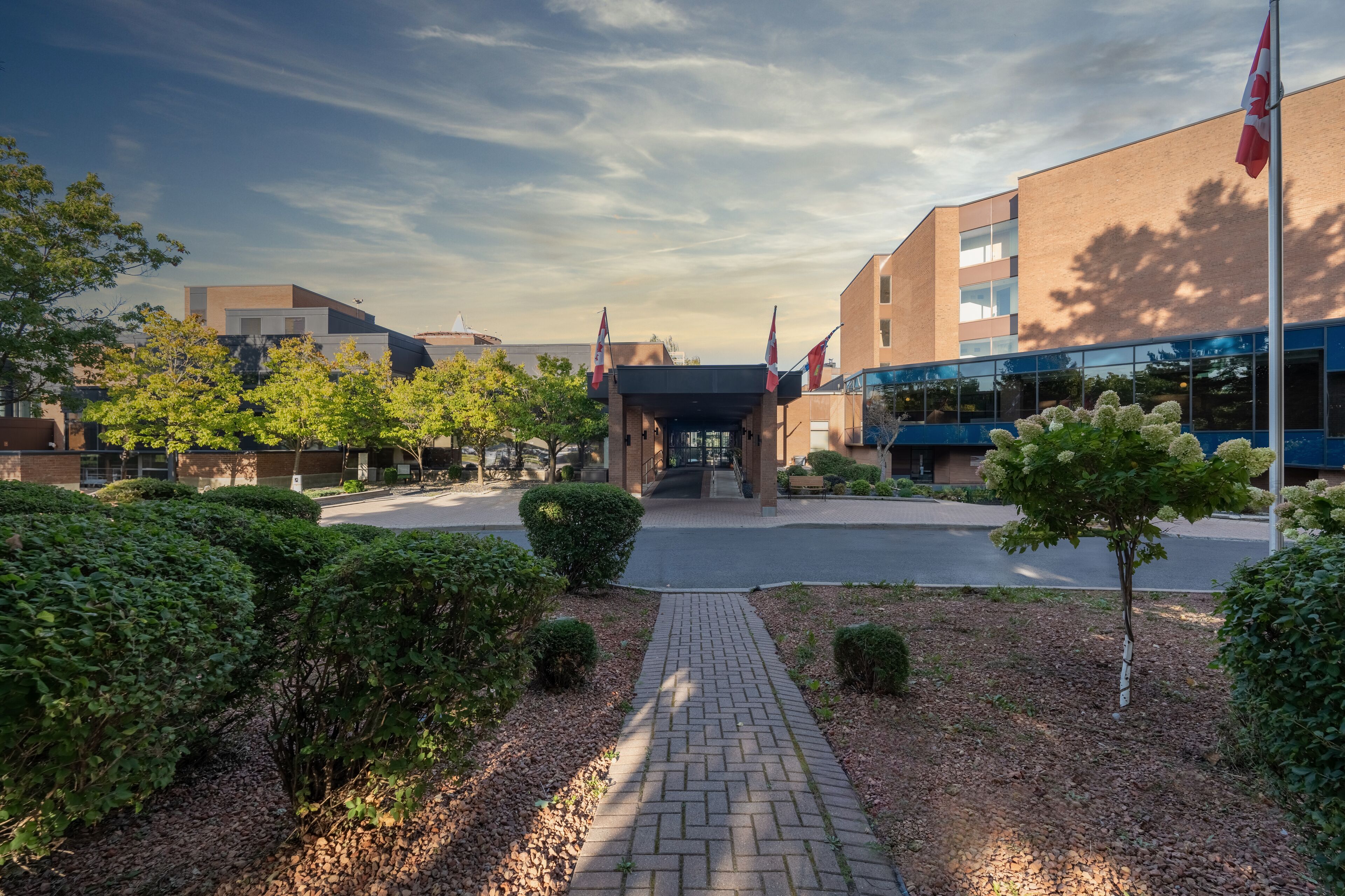 A modern building with a brick facade, a covered entrance, and multiple flags.