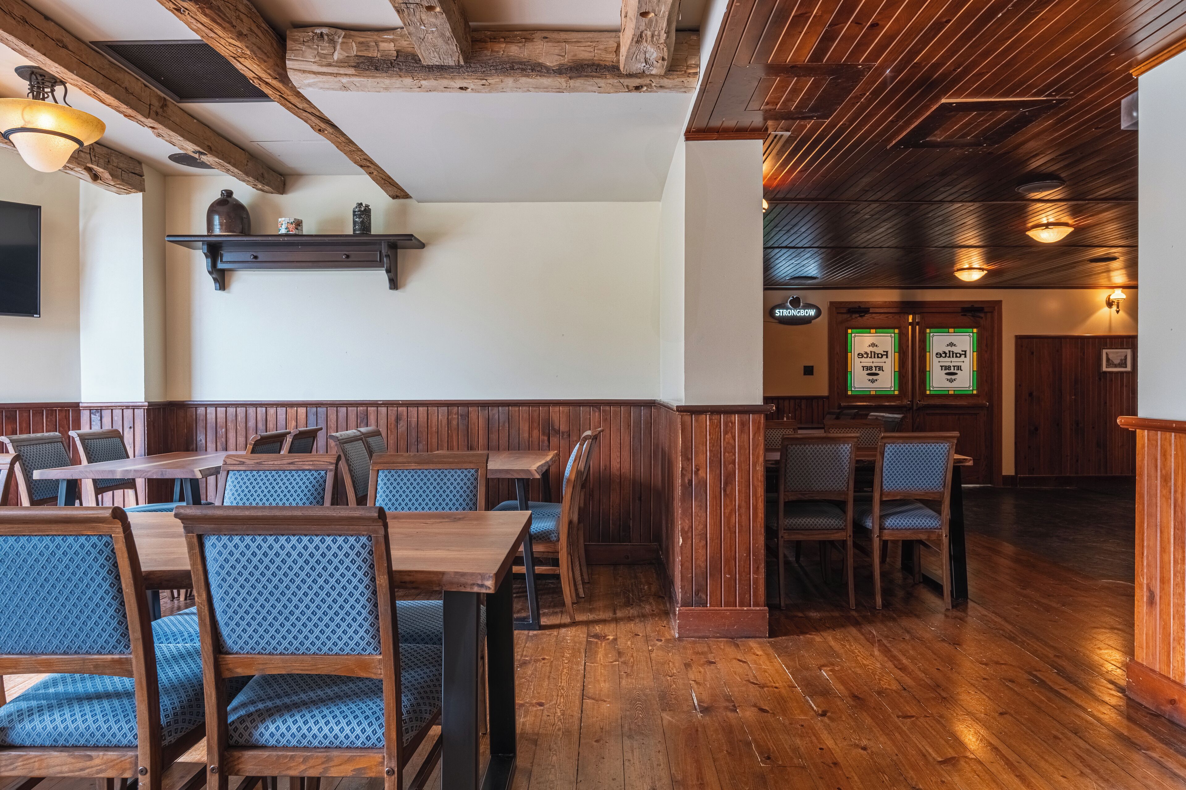 Interno di un ristorante con tavoli e sedie in legno, soffitto in legno ed scaffali a parete.
